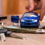 A toy car is driven over a stack of money.